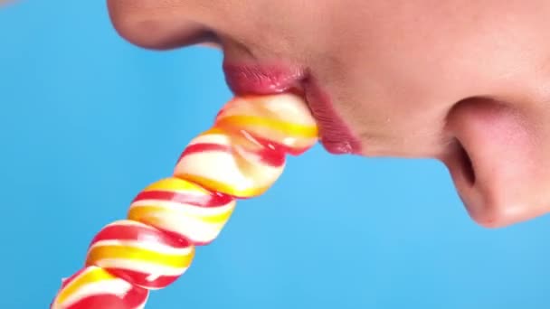 Vertical close-up, female sexy lips with red lipstick suck big spiral oblong candy lollipop. copy space. blue background — Stock Video