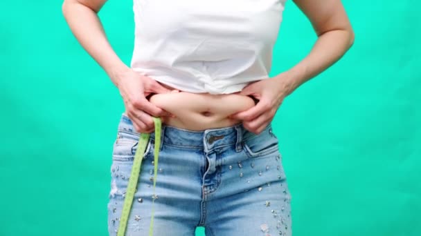 Una mujer en el fondo de cinta métrica y manzana verde, toca y mide su estómago grasiento, control de peso corporal, ropa alrededor del abdomen — Vídeos de Stock