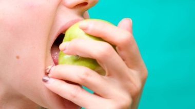 Yakın plan bir kadın yeşil arka planda yeşil elma yer, sağlıklı gıda, kilo kaybı ve sağlık dişleri kavramı