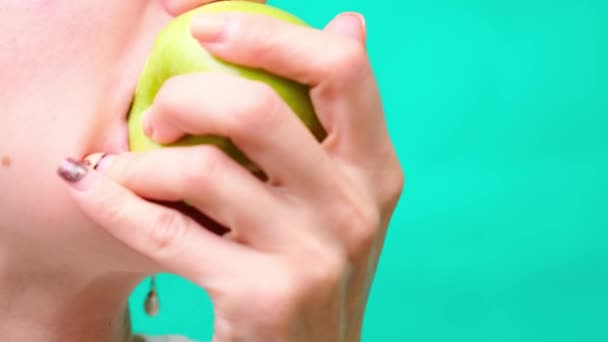 Una mujer de cerca come una manzana verde sobre un fondo verde, el concepto de una alimentación saludable y la pérdida de peso y dientes de salud — Vídeos de Stock