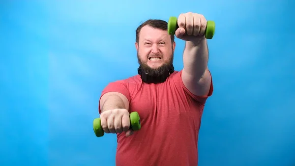 Thick bearded nice bodybuilder in pink T-shirt with very small dumbbells is very tense doing exercises — Stock Photo, Image