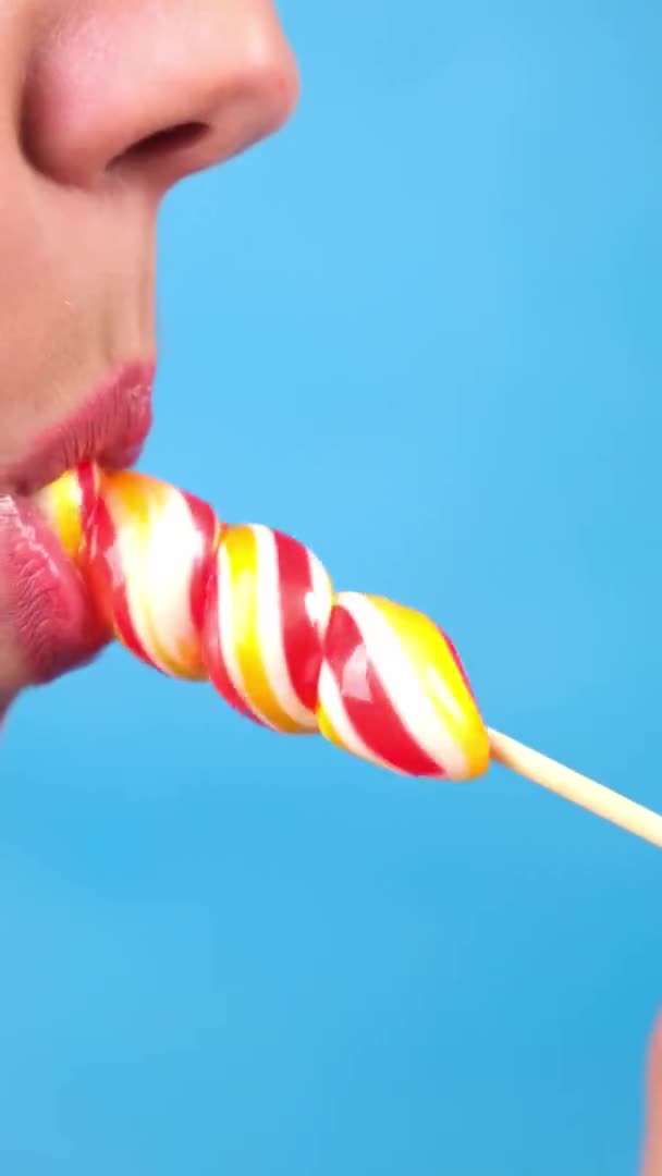 Vertical close-up, female sexy lips with red lipstick suck big spiral oblong candy lollipop. copy space. blue background — Stock Video