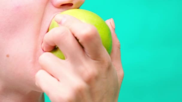 Eine Frau aus nächster Nähe isst einen grünen Apfel auf grünem Hintergrund, das Konzept einer gesunden Ernährung und Gewichtsverlust und gesunde Zähne — Stockvideo