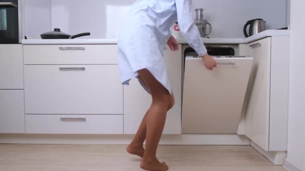 Une femme en vêtements de maison danse dans la cuisine et enlève la vaisselle propre du lave-vaisselle — Video