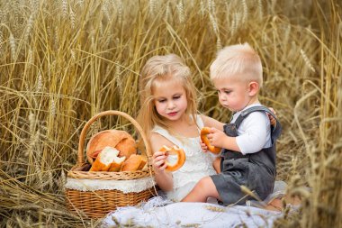 Erkek ve kız buğday tarlasında piknikte pişmiş yiyecekler yiyorlar.