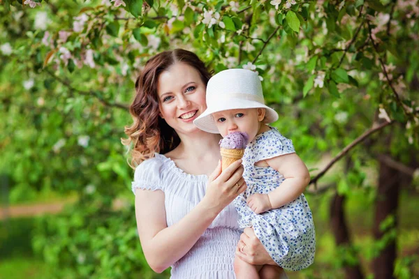 Young beautiful mom with daughter in hat eating ice cream in park in spring — Stock Photo, Image