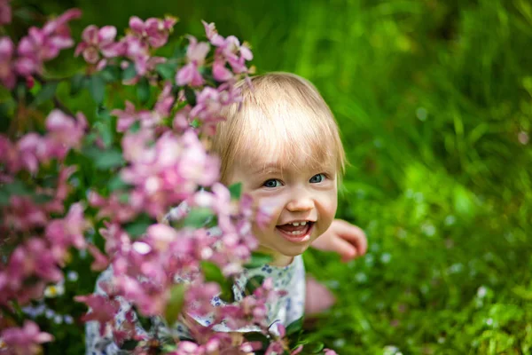 Close-up portret van een 1-2 jaar oud meisje buiten in een tuin met roze bloemen in de bomen. — Stockfoto
