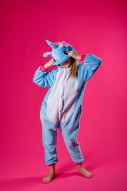 Çekici kız tek boynuzlu at kostümü içinde şakacı poz veriyor. Kigurumi 'de pembe arka planda eğlenen duygusal bir kadının stüdyo fotoğrafı..