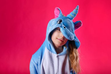 Çekici kız tek boynuzlu at kostümü içinde şakacı poz veriyor. Kigurumi 'de pembe arka planda eğlenen duygusal bir kadının stüdyo fotoğrafı..