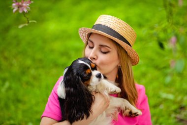 Baharda parkta küçük bir şövalye kralı Charles Spaniel 'i öpen bir köpek sahibinin yakın plan portresi. Genç sarışın, köpeğiyle eğleniyor..