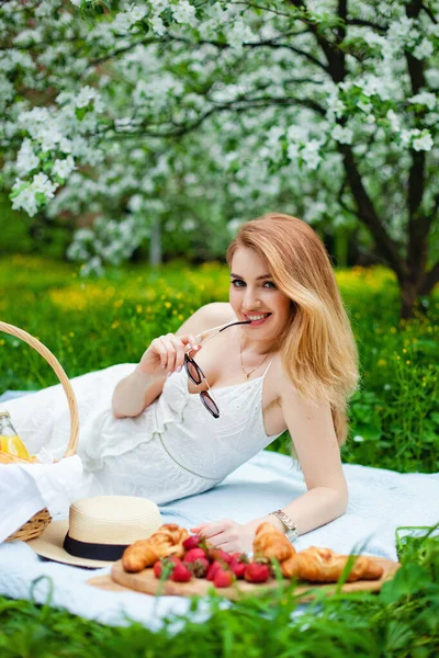 portrait oportrait of a girl in a white dress and sunglasses at a picnic in a blooming orchard. spring time