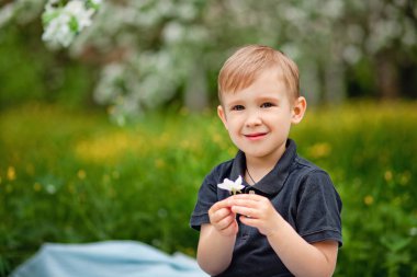 Mutlu, beyaz bir çocuk bahar bahçesinde piknik yapıyor. Çilekli güzel bir çocuk, piknikte kruvasan. Çocukluk, mutluluk kavramı..
