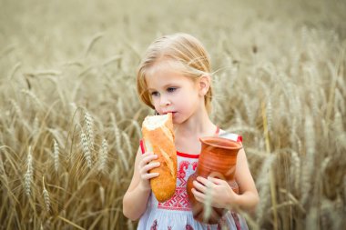 Elinde kahverengi sürahi ve ekmek olan küçük bir kızın portresi. Bir kız kırsalda buğday tarlasında poz veriyor..