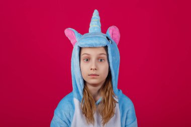 Çekici kız tek boynuzlu at kostümü içinde şakacı poz veriyor. Kigurumi 'de pembe arka planda eğlenen duygusal bir kadının stüdyo fotoğrafı..