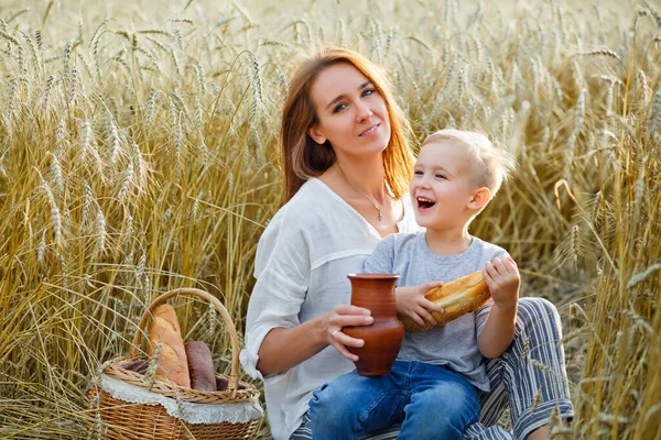 family picnic in nature on a family picnic in nature on a summer evening. mother and son eat bread, drink milk from a ceramic jug in a wheat field