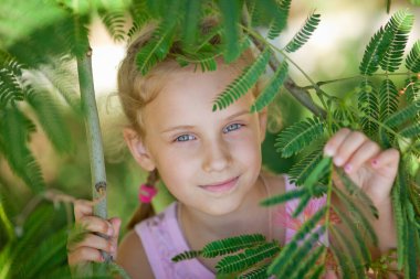 Bir çocuğun yakın plan portresi. Çiçek açmış pembe bir akasyanın yanında yaz esprisi yapan küçük kız. Albizia julibrissin