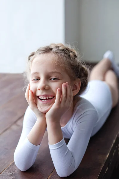 A charming little girl in a white gymnastic costume is training in rhythmic gymnastics. A little girl is doing exercises on the floor. For a child, the concept