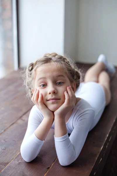 A charming little girl in a white gymnastic costume is training in rhythmic gymnastics. A little girl is doing exercises on the floor. For a child, the concept