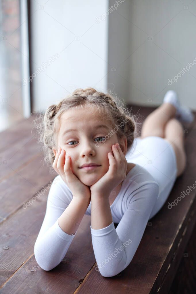 A charming little girl in a white gymnastic costume is training in rhythmic gymnastics. A little girl is doing exercises on the floor. For a child, the concept