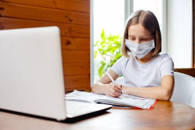 Evde eğitim. Bir kız, bir öğretmen ve sınıf ile okul dersinin online görüntülü sohbeti sırasında dizüstü bilgisayarla masada oturuyor. Uzaktan eğitim kavramı. Karantinada kendini izole etme