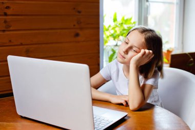 Evde eğitim. Bir kız, bir öğretmen ve sınıf ile okul dersinin online görüntülü sohbeti sırasında dizüstü bilgisayarla masada oturuyor. Uzaktan eğitim kavramı. Karantinada kendini izole etme