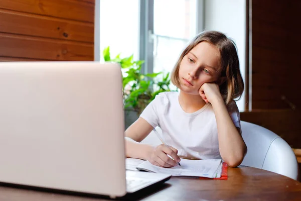 Home schooling. A girl is sitting at a table with a laptop during an online video chat of a school lesson with a teacher and class. Concept of distance education. Self-isolation in quarantine