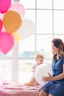Genç bir anne ve kız ellerinde balonlarla pencere eşiğinde oturuyorlar. İyi tatiller. Anneler Günü..