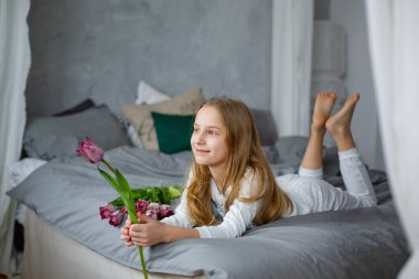 Pijamalı bir bebek bir buket pembe lale ile oynar. Yatak odasında küçük bir çocuk. Çocuk çiçeklerle eğleniyor.