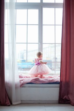 Pencere kenarında oturan pembe elbiseli mutlu bir sarışının portresi. Evde rahat..