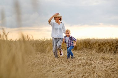 Mutlu anne ve oğul yazın buğday tarlasında koşuyor.