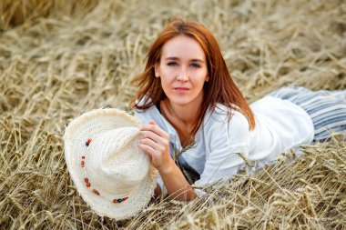 Buğday tarlasında yatan ve yaz mevsiminde otların üzerinde poz veren bir kız. Doğada dinlenmek. Genç kadın sahada poz veriyor.