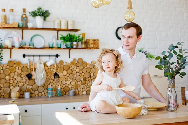Caucasian dad and daughter, funny dad and girl hugging and cooking together in the kitchen in a bright kitchen, lifestyle and father's Day, single parents