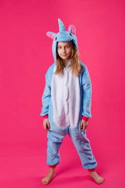 Çekici bir kız tek boynuzlu at kostümü içinde şakacı bir şekilde poz veriyor. Tam kapüşonlu duruyor. Kigurumi 'de pembe arka planda eğlenen duygusal bir kadının stüdyo fotoğrafı..