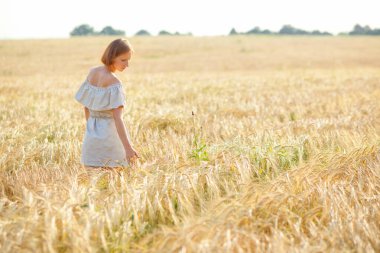 Kafasında hasır şapka olan genç bir kız buğday tarlasında dans ediyor. Elini kulakların üzerinden geçiriyor. Sırtı kameraya dönük duruyor..