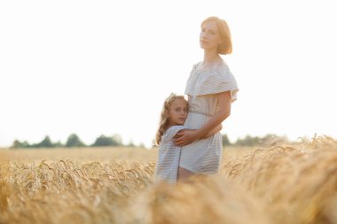 Güzel kızıl saçlı bir anne ve kızı güneşli bir günde buğday tarlasında birbirlerine sarılıyorlar..