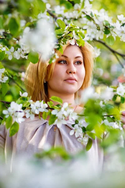 A beautiful blonde girl holds a flower branch of an Apple tree in her hands. Close-up Portrait of a young girl in a blooming garden.