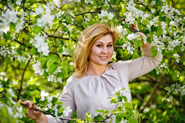 A beautiful blonde girl holds a flower branch of an Apple tree in her hands. Close-up Portrait of a young girl in a blooming garden.