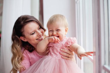 Anne pembe elbiseli kızıyla pencerede oynuyor. Anneler Günü.