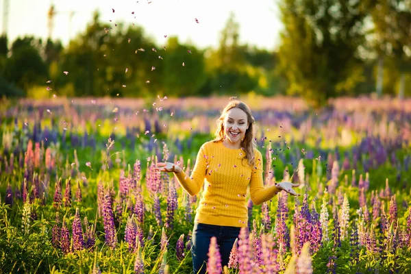 黄色のセーターを着た幸せな女性がジャンプし 日没時に紫色のラインが咲く分野での生活を楽しんでいます 少女は花びらを投げ出し — ストック写真