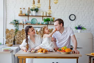 Kahvaltı sırasında mutfakta poz veren mutlu anne, kız ve babanın aile portresi. Lezzetli kurabiyeler, kurabiyeler. İyi bir evlilik, birbirinizi sevin.