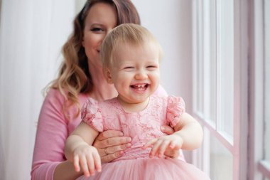 Anne pembe elbiseli kızıyla pencerede oynuyor. Anneler Günü.