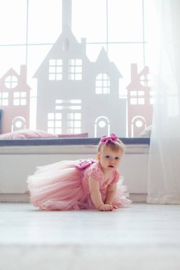 Pencere kenarında oturan pembe elbiseli mutlu sarışın bir kızın portresi.