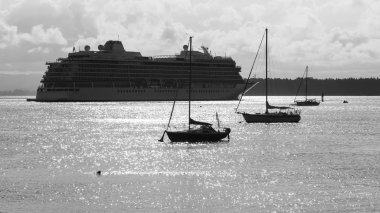 Limanın parlak sularında, ön planda küçük yelkenlileri olan büyük bir yolcu gemisi. Siyah ve beyaz. 