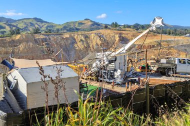 Mineral exploration. A portable drilling rig taking samples on the rim of the open-cast Martha gold mine in Waihi, New Zealand clipart