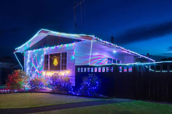 Gece bir banliyö evi ve bahçesinde renkli Noel süslemeleri (sicim ışıkları ve projeksiyonlu ışıklar) 