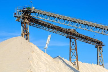 A giant outdoor pile of salt beneath a conveyor belt at a salt refinery
