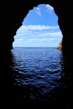 View from inside a sea cave (Orua sea cave on the Coromandel Peninsula, New Zealand) looking out at the ocean. A tour boat is visible in the distance clipart