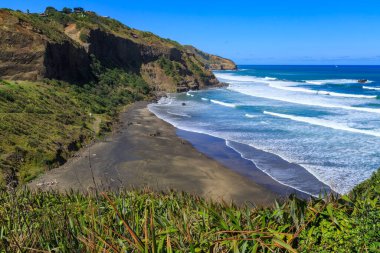 Muriwai, Yeni Zelanda yakınlarındaki Maori Körfezi 'nde ağır sörf yapılan siyah bir kumsal.