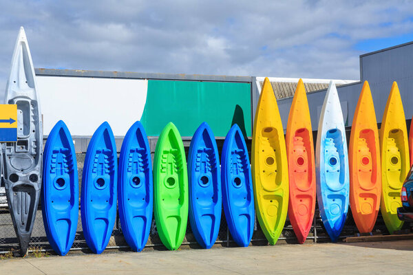 A colorful row of plastic kayaks, standing upright along a fence