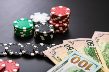 Siyah arka planda yığınla poker fişi ve dolar banknotları. Dürt